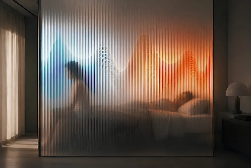 A person sleeps in a dim bedroom seen through a fluted glass panel, with warm-to-cool color waves projected across the glass suggesting room temperature.