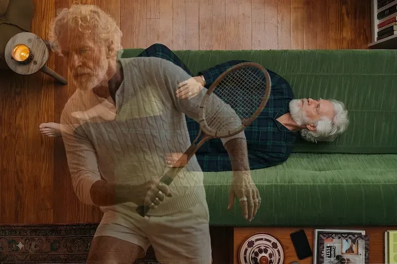 A grey-haired man lies resting on a green sofa while a ghosted double exposure shows him mid-swing with a tennis racket, contrasting passive and active rest.