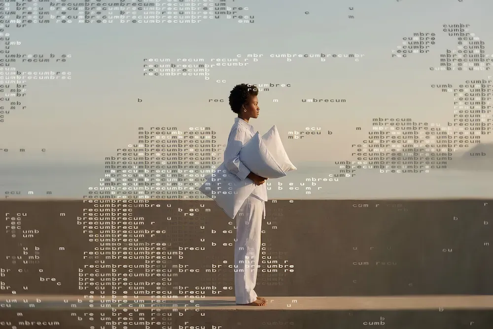A woman in white pajamas stands holding a pillow, the sky around her filled with scattered, jumbled letters like mental static.