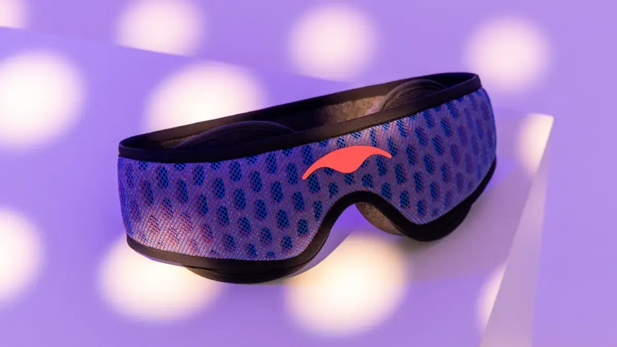 Manta PRO Sleep Mask lying on a white surface, enlightened by light purple light.