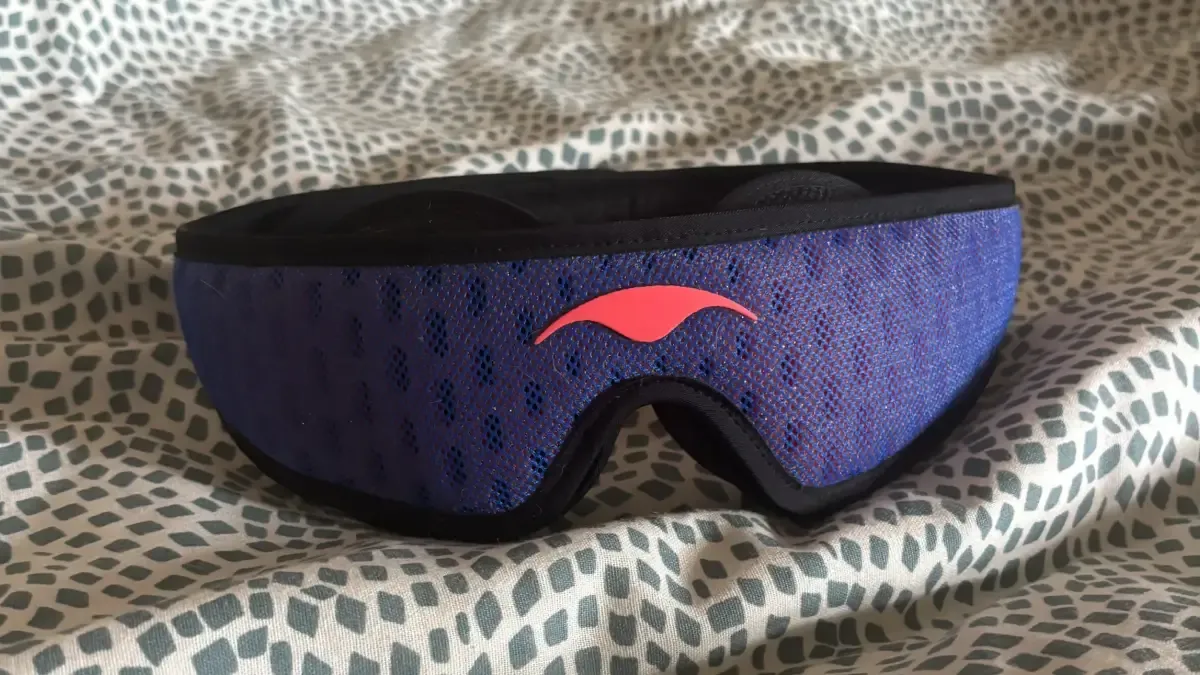 A Manta PRO Sleep Mask lying on a bed with textured bedding.
